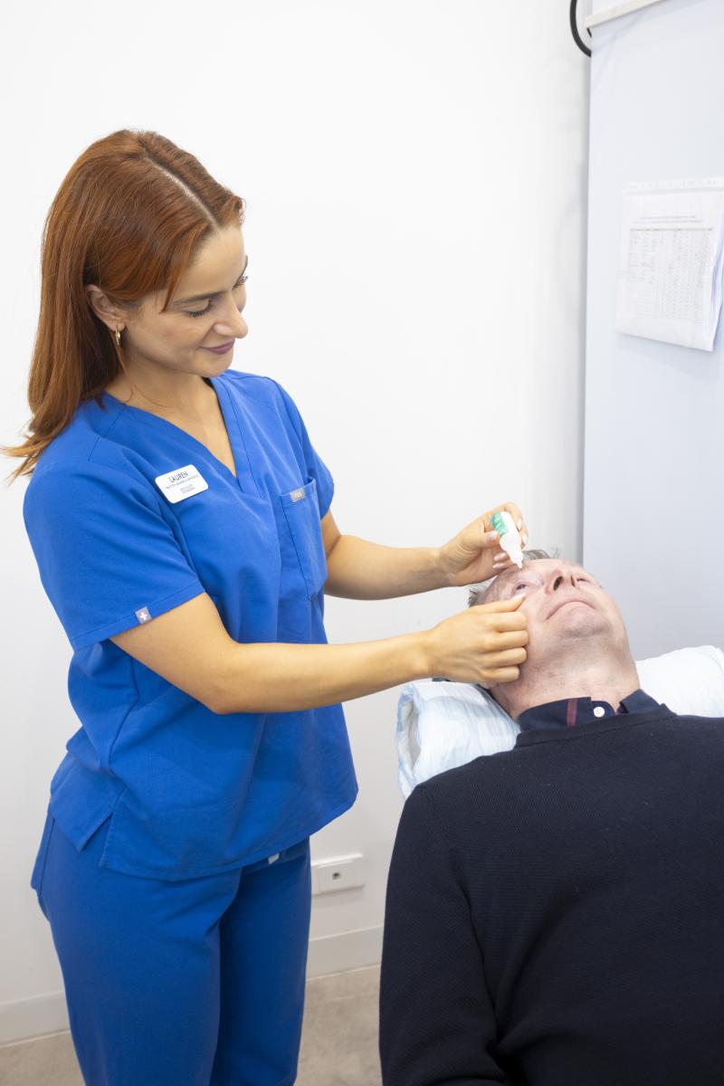Clinician in blue scrubs applying eye drops to a patient during an eye clinic appointment